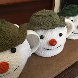 May include: Three knitted teapot cozies in the shape of snowmen. Each cozy is white with a green knitted hat and a red pom-pom nose.