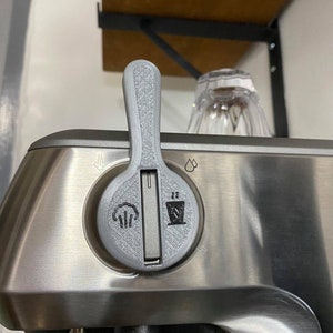 May include: A silver kitchen appliance with a gray control knob. The knob has a steam icon, a drip icon, and two icons that look like a hand and a trash can.