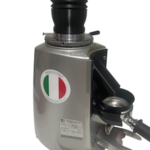 May include: Silver espresso grinder with a black hopper and portafilter holder. The grinder has a sticker that says "Made in Italy" with the Italian flag. The grinder is labeled "MAZZER LUIGI Spa MINI BEAL".