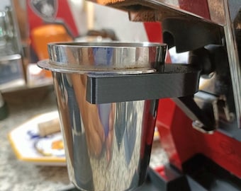 Könnte beinhalten: Ein Edelstahl-Siebträgerhalter an einer rot-silbernen Espressomaschine befestigt. Der Siebträger ist mit gemahlenem Kaffee gefüllt. Die Maschine hat einen schwarzen Sockel und einen silbernen Deckel.