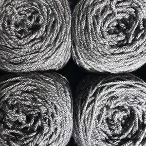 May include: Four gray yarn skeins are neatly arranged, filling the frame. The yarn is tightly wound, revealing a spiral pattern. The color is a solid, medium gray, with a slight sheen. The yarn appears soft and suitable for knitting or crochet projects.