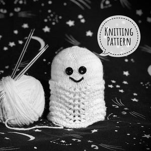 May include: A white knitted ghost with black button eyes and a smiling mouth. The ghost is sitting on a black background with white stars. The text "Knitting Pattern" is in a speech bubble above the ghost.