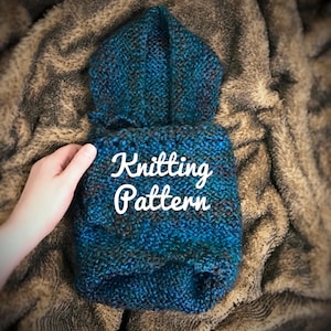 May include: A blue knitted hooded garment with a white "Knitting Pattern" text overlay. The garment is lying on a brown fuzzy surface.