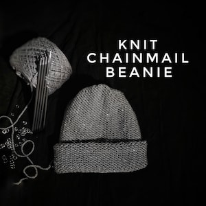 May include: A grey knitted beanie with a chainmail pattern. The beanie is on a black background with knitting needles and yarn.