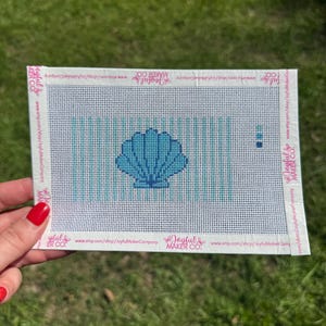 May include: A rectangular needlepoint canvas featuring a centered blue seashell design against a background of vertical light blue stripes. The white border includes the repeating text Joyful Maker Co. and the URL etsy.com/shop/JoyfulMakerCo.