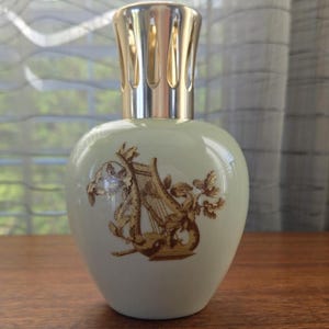 May include: A pale green decorative bottle with a gold-colored metal top. The bottle features a gold harp and floral design. The bottle is sitting on a wooden surface.