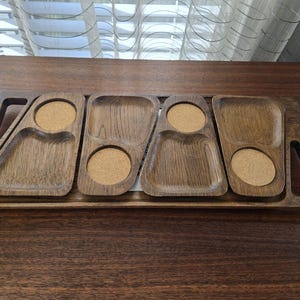 May include: A wooden serving tray with four compartments and two circular cutouts for coasters. The tray is made of dark brown wood and has a rectangular shape with handles on each end. The coasters are a light brown color.