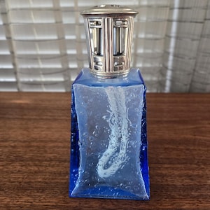 以下が含まれることがあります： 銀色の金属製のトップが付いた青いガラスのオイルランプ。 ランプは長方形で、表面はテクスチャ加工されています。 銀色のトップには装飾的なデザインが施されています。