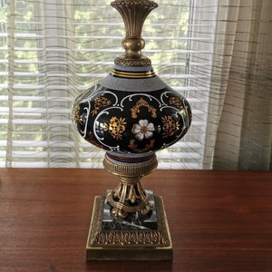 May include: A black and white ceramic table lamp with gold accents and a marble base. The lamp has a floral design and a round, bulbous shade.