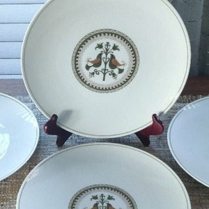 May include: Three white ceramic dinner plates with a green and brown floral design featuring two birds. The design is centred on each plate.