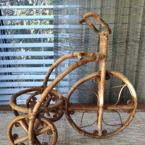 May include: A brown bamboo tricycle with a woven design. The tricycle has three wheels and a handlebar. The wheels are made of woven bamboo and have a circular design.