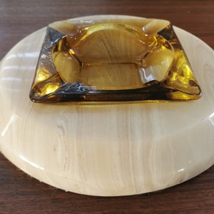 May include: A round, white, marble ashtray with a square, amber glass inset. The ashtray has a swirl pattern.
