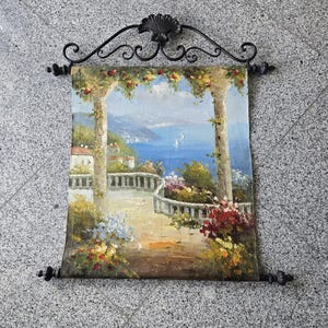 Peut inclure: Une tenture murale décorative avec une peinture de paysage d'une scène côtière. L'œuvre représente un balcon, des fleurs et une mer bleue. Elle est encadrée par un support en métal noir, ajoutant une touche d'élégance.