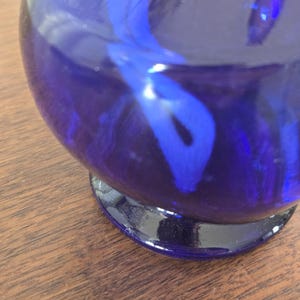 Pu&ograve; includere: Un vaso di vetro blu cobalto con corpo arrotondato e base scura. L'interno presenta un design a spirale blu pi&ugrave; chiaro. Il vaso &egrave; appoggiato su una superficie di legno.