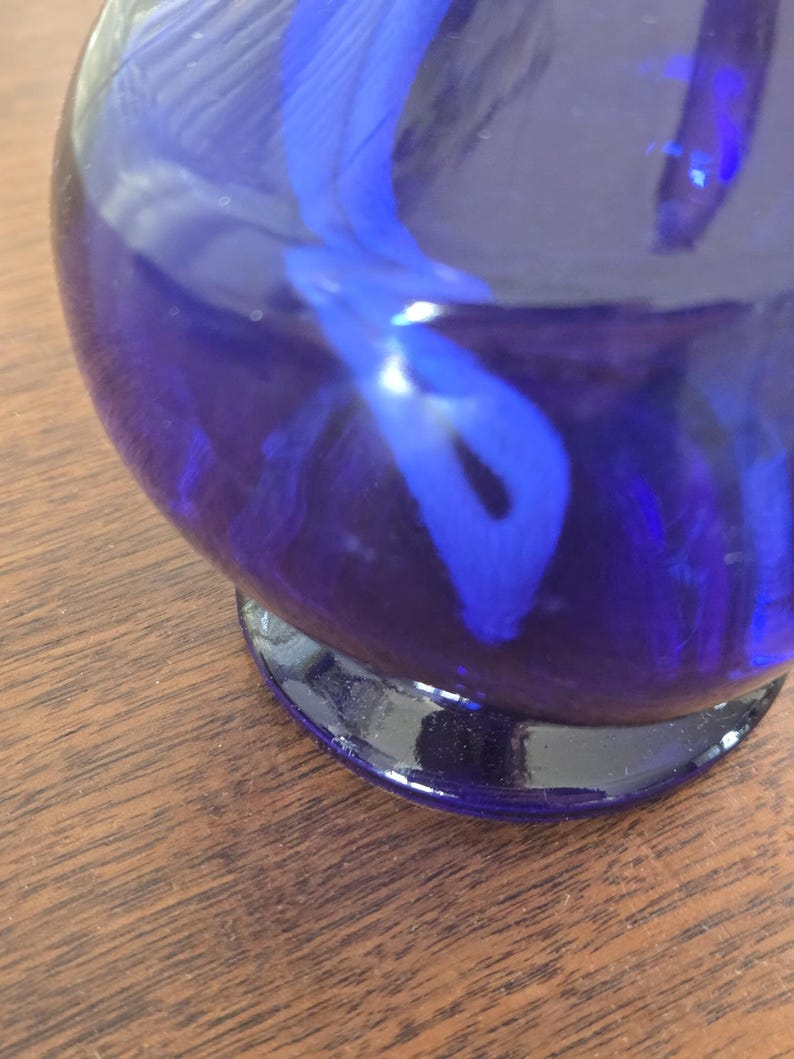 Pu&ograve; includere: Un vaso di vetro blu cobalto con corpo arrotondato e base scura. L'interno presenta un design a spirale blu pi&ugrave; chiaro. Il vaso &egrave; appoggiato su una superficie di legno.
