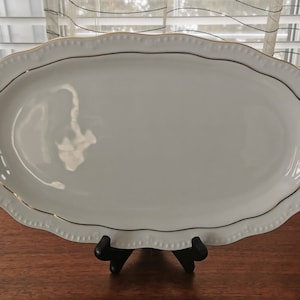 May include: White oval serving platter with a gold rim and a scalloped edge.