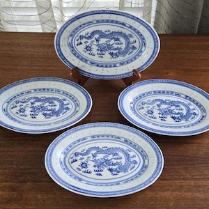 May include: Set of four oval ceramic plates featuring a blue and white dragon design. The plates have a white background with a blue border and a blue dragon in the centre.