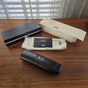 Peut inclure: Un étui à stylo en cuir noir avec un accent argenté, une boîte noire avec une rayure blanche, une boîte crème et une pochette crème avec un guide de service. Les boîtes et la pochette portent le logo Montblanc.