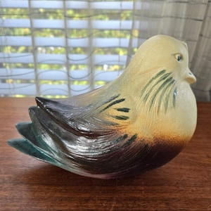 May include: A ceramic bird figurine with a yellow, brown, green, and purple glaze. The bird is sitting on a wooden surface.