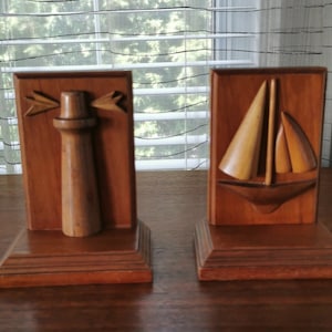 May include: A pair of wooden bookends featuring a carved lighthouse and sailboat. The bookends are a dark brown color and have a natural wood finish.