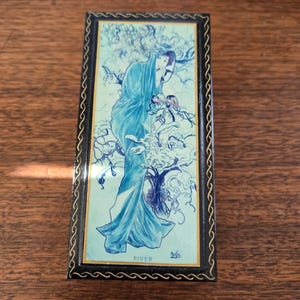 May include: Rectangular black box with a decorative lid featuring a blue and white illustration of a woman in flowing robes. The artwork is framed with a black border and a gold trim. The word "RIVER" is visible.