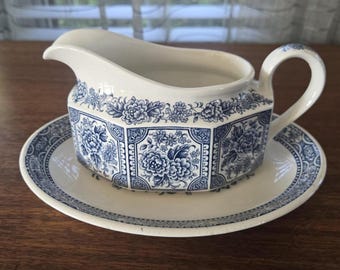 May include: A white gravy boat and saucer set with a blue floral design. The gravy boat has a spout and handle, and the saucer is round. The set is likely vintage or antique.
