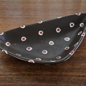 Peut inclure: Un plat en céramique triangulaire marron foncé orné de points rouges bordés de blanc. Le plat est conçu pour servir des collations ou de petits articles. Les points sont espacés uniformément sur la surface.