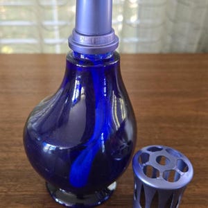 Pu&ograve; includere: Un flacone di profumo in vetro blu cobalto con tappo coordinato e un manicotto perforato decorativo separato. Il flacone ha una forma bulbosa con un collo lungo e un design a spirale blu scuro. Il tappo e il manicotto sono di una tonalit&agrave; di blu pi&ugrave; chiara.
