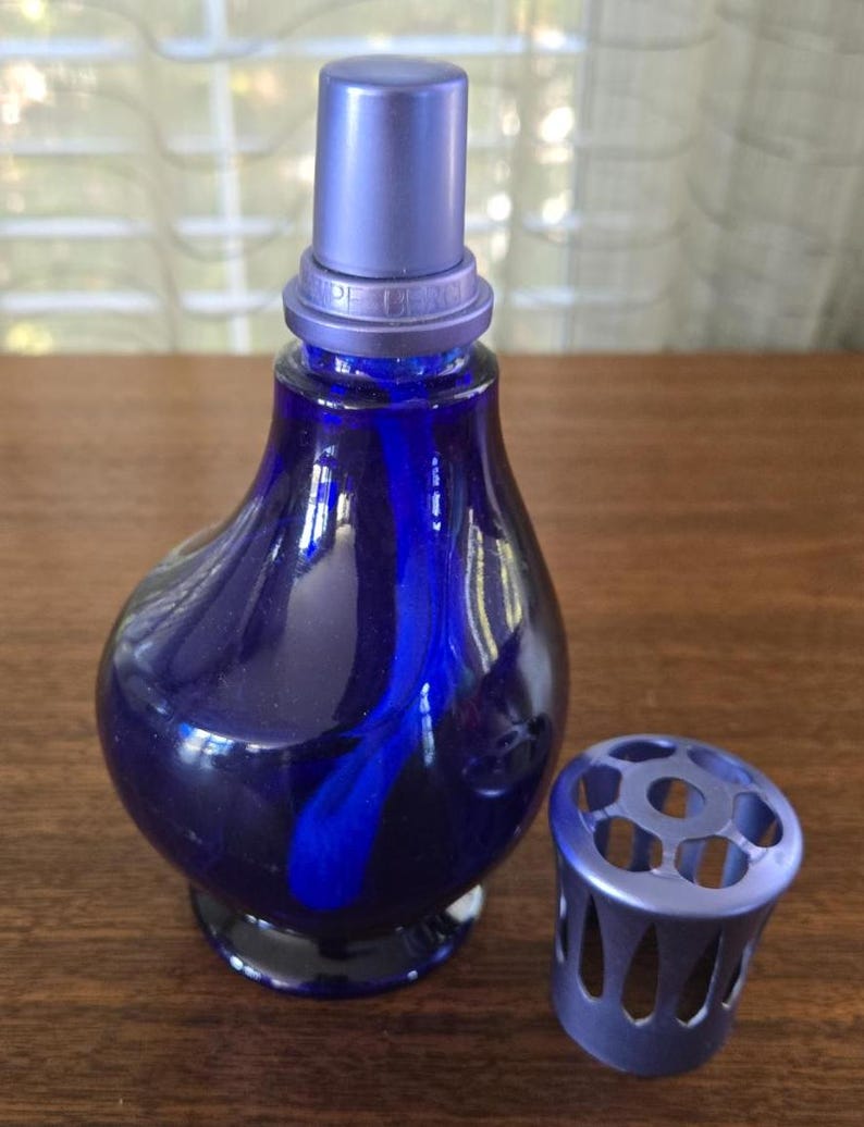 Pu&ograve; includere: Un flacone di profumo in vetro blu cobalto con tappo coordinato e un manicotto perforato decorativo separato. Il flacone ha una forma bulbosa con un collo lungo e un design a spirale blu scuro. Il tappo e il manicotto sono di una tonalit&agrave; di blu pi&ugrave; chiara.