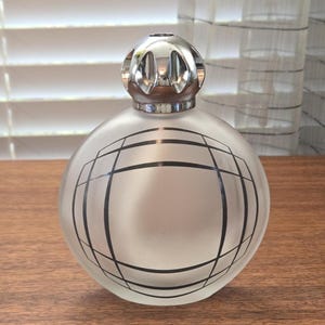 May include: A spherical, frosted glass fragrance lamp featuring a black geometric grid pattern on its front surface. The lamp is topped with a polished, silver-coloured metal burner cap that has a series of vertical cutouts around its rounded dome.