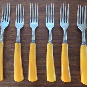 Peut inclure: Ensemble de six fourchettes vintage avec des manches en plastique jaune. Les fourchettes ont une finition argentée et sont en bon état.