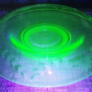 May include: A green glass bowl with an etched floral design. The bowl has a raised center and a scalloped edge.