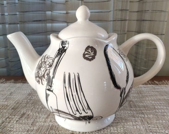 Puede incluir: Tetera de cerámica blanca con un diseño en blanco y negro de utensilios de cocina. La tetera tiene un cuerpo redondo y una tapa con un pomo en la parte superior. El diseño incluye un tenedor, un cuchillo y una cuchara.