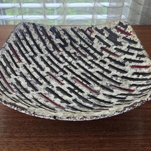 May include: A square ceramic serving dish with a white base and black and red lines. The dish has a textured surface and a slightly curved shape.