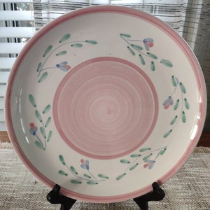 May include: A white ceramic serving platter with a pink rim and a floral design. The design features green leaves and blue flowers.