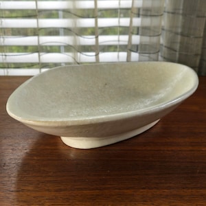 May include: A white ceramic oval serving bowl with a textured surface. The bowl has a slightly raised base.
