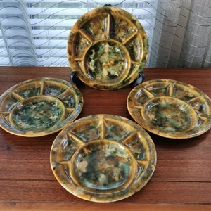 May include: Set of four ceramic divided serving plates with a green and yellow glaze. The plates are circular with a central well and six smaller compartments around the edge.