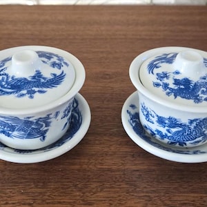 Peut inclure: Deux tasses à thé blanches avec des motifs de dragons bleus et blancs. Les tasses à thé ont des couvercles et sont posées sur des soucoupes assorties.