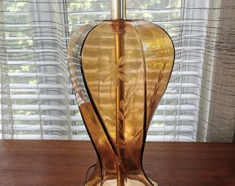 May include: A vintage amber glass table lamp with an etched floral design. The lamp has a brass base with a square shape and three feet.