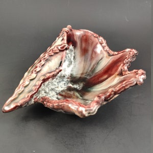May include: A ceramic bowl with a unique, organic shape and a mottled glaze in shades of red, white, and green.