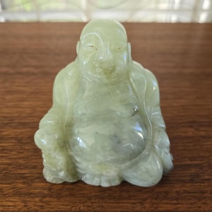 Puede incluir: Una escultura de jade verde de un Buda sonriente sentado con las manos en el regazo.