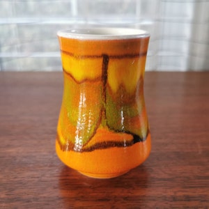 May include: A small, orange, yellow and green ceramic vase with a flared base. The vase has a glossy finish and a unique abstract design.