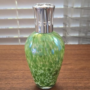 May include: A teardrop-shaped glass fragrance lamp featuring a speckled pattern of light and dark green spots against a white background. The vessel is topped with a polished silver-colored metal crown cap with vertical cutouts for ventilation.