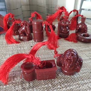 Peut inclure: Une collection de petites figurines brillantes, brun rougeâtre, dont un homme souriant, un puits et un tonneau, chacune ornée de pompons rouges vifs. Les figurines sont disposées sur une surface texturée.