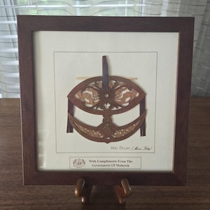 May include: A framed wooden cutout of a traditional Malaysian kite, called a Wau Bulan, with the text "Wau Bulan (Moon Kite)" and "With Compliments From The Government Of Malaysia".