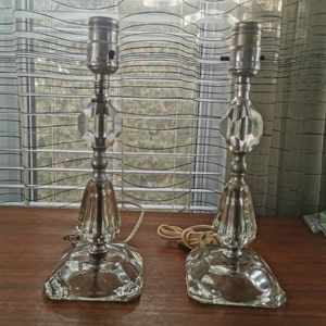 May include: A pair of crystal table lamps with silver accents and clear glass bases. The lamps have a vintage style and are perfect for adding a touch of elegance to any room.