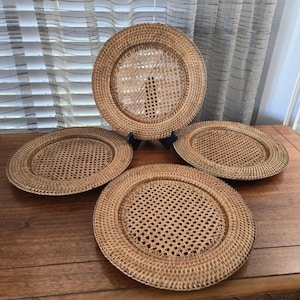 Könnte beinhalten: Vier gewebte Rattan-Servierplatten mit natürlichem Finish. Die Servierplatten haben eine runde Form mit gewebter Mitte und einem durchgehenden Rand. Eine Servierplatte steht auf einem schwarzen Ständer. Die Servierplatten befinden sich auf einer Holzoberfläche.