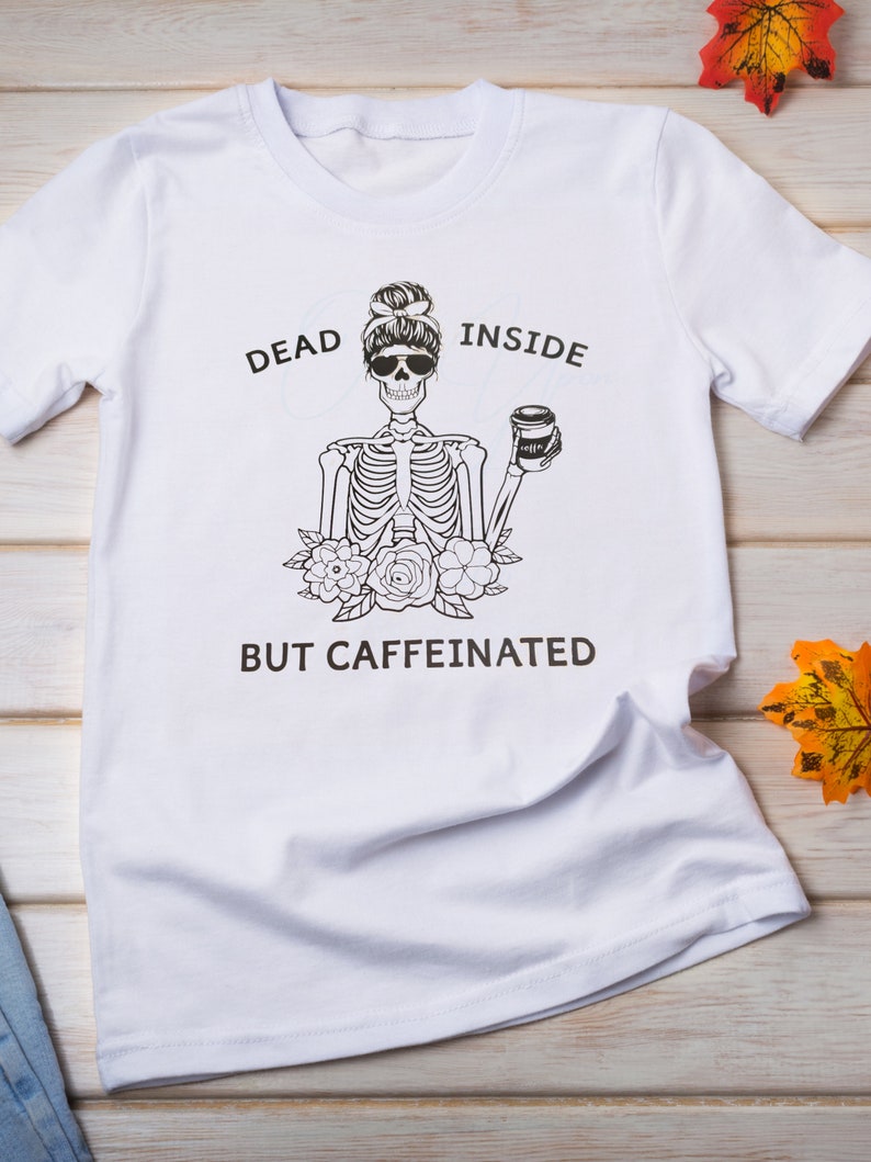 May include: White t-shirt with a black and white skeleton graphic holding a coffee cup. The text "Dead Inside But Caffeinated" is printed on the shirt.