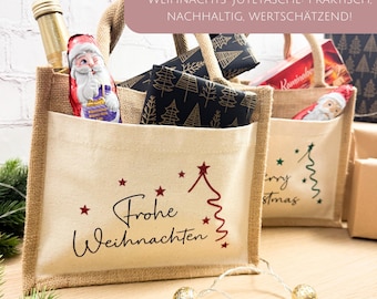 May include: Two jute tote bags with Christmas designs. One bag features "Frohe Weihnachten" text and a red tree graphic. The other has "Merry Christmas" text and a green tree. Both bags have a front pocket and rope handles.