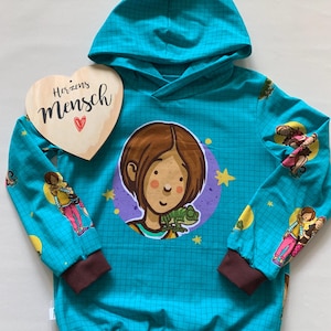 Könnte beinhalten: Türkisfarbener Kapuzenpullover mit Gittermuster, mit einem Cartoon-Mädchen mit Chamäleon und dem Text "Herzens Mensch" auf einem Holzherz. Die Ärmel haben Illustrationen von Mädchen und Sternen, mit braunen Bündchen und Saum.